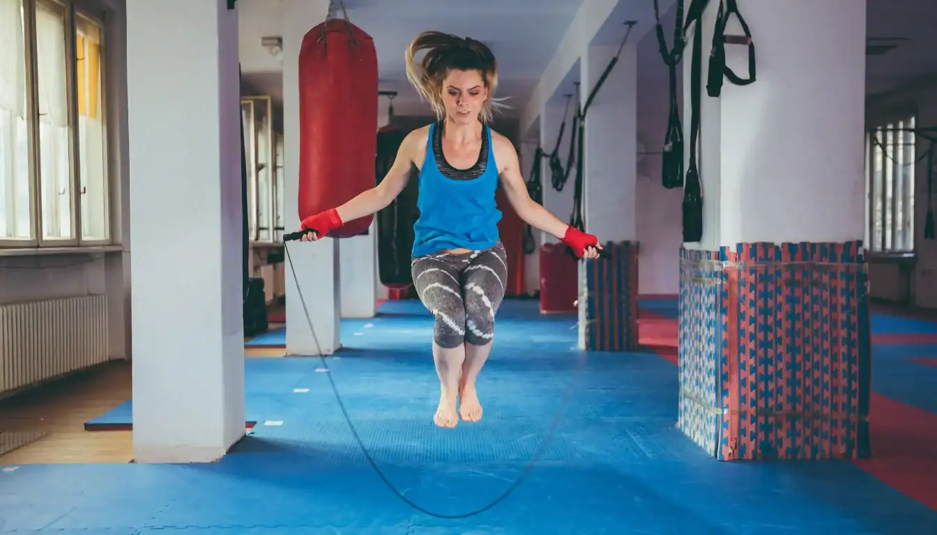Energetic adult woman jumping rope using a jump rope calorie calculator in a modern home gym with natural light.