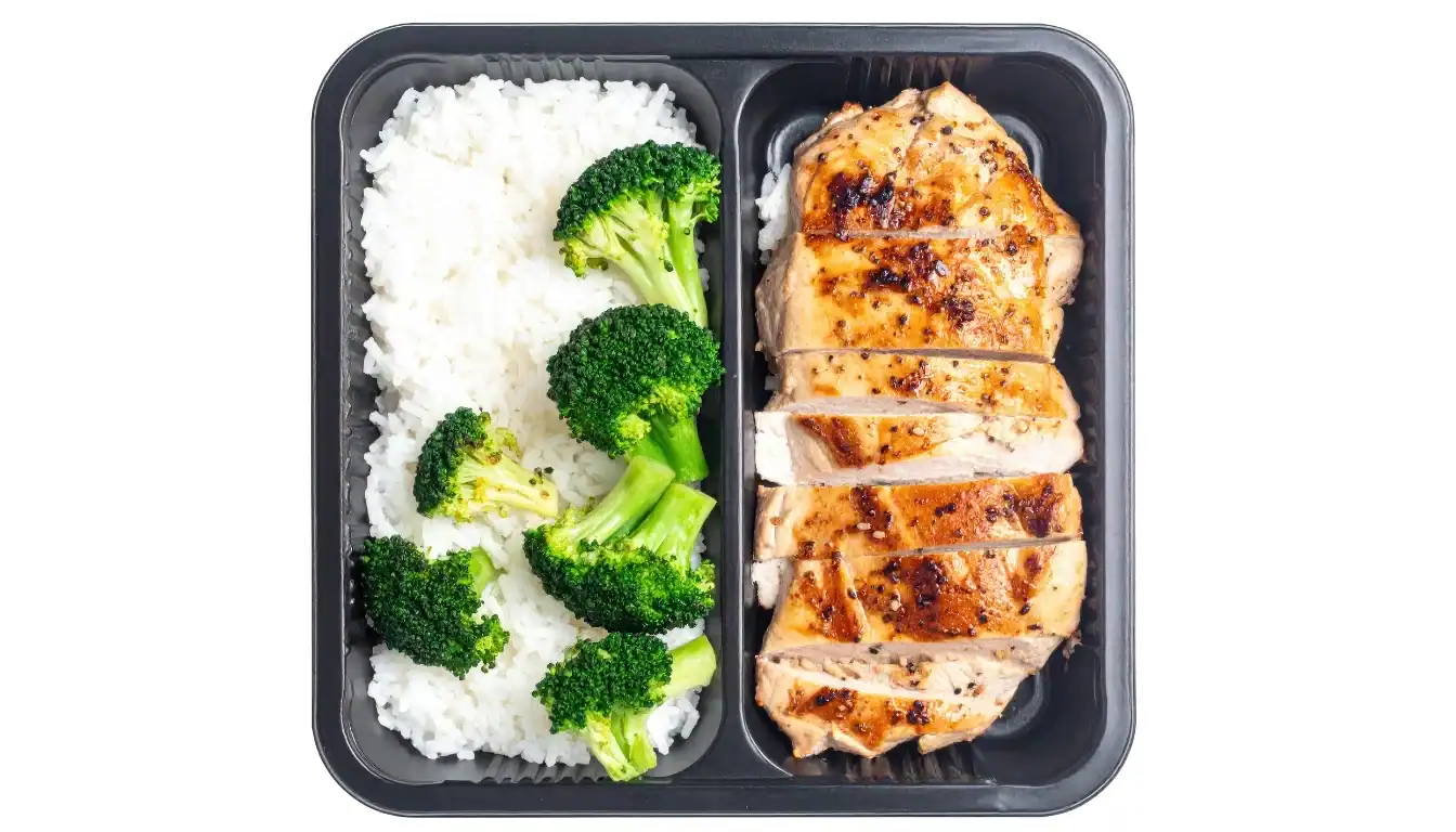 Balanced meal prep containers with rice for weight loss - rice, lean meat, and colorful vegetables arranged on a kitchen counter